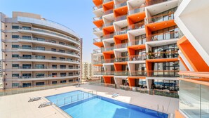 Piscina no terraço com espreguiçadeiras, cercada por edifícios altos com sacadas.