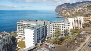 Un hotel moderno de varios pisos, con estacionamiento y vistas al mar y un paisaje montañoso.