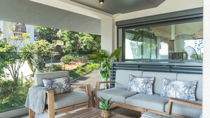 Un salón moderno con un sofá, sillones y una mesa de centro. Se ve una ventana grande con vistas a zonas verdes y edificios.