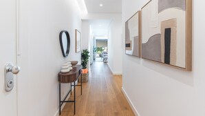 Un pasillo con piso de madera, una puerta con picaporte moderno, una mesita con objetos decorativos y cuadros en las paredes.