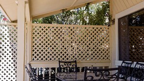 Un patio al aire libre con mesa y sillas de madera, una celosía y vistas al verdor.