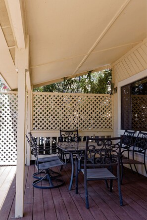 An outdoor patio with a wooden table and chairs, a lattice screen, and a view of greenery.