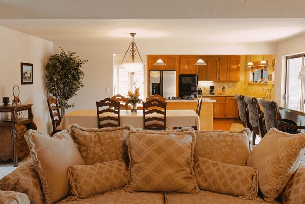 A cozy living room with a sofa, a dining table with chairs, and a kitchen in the background.