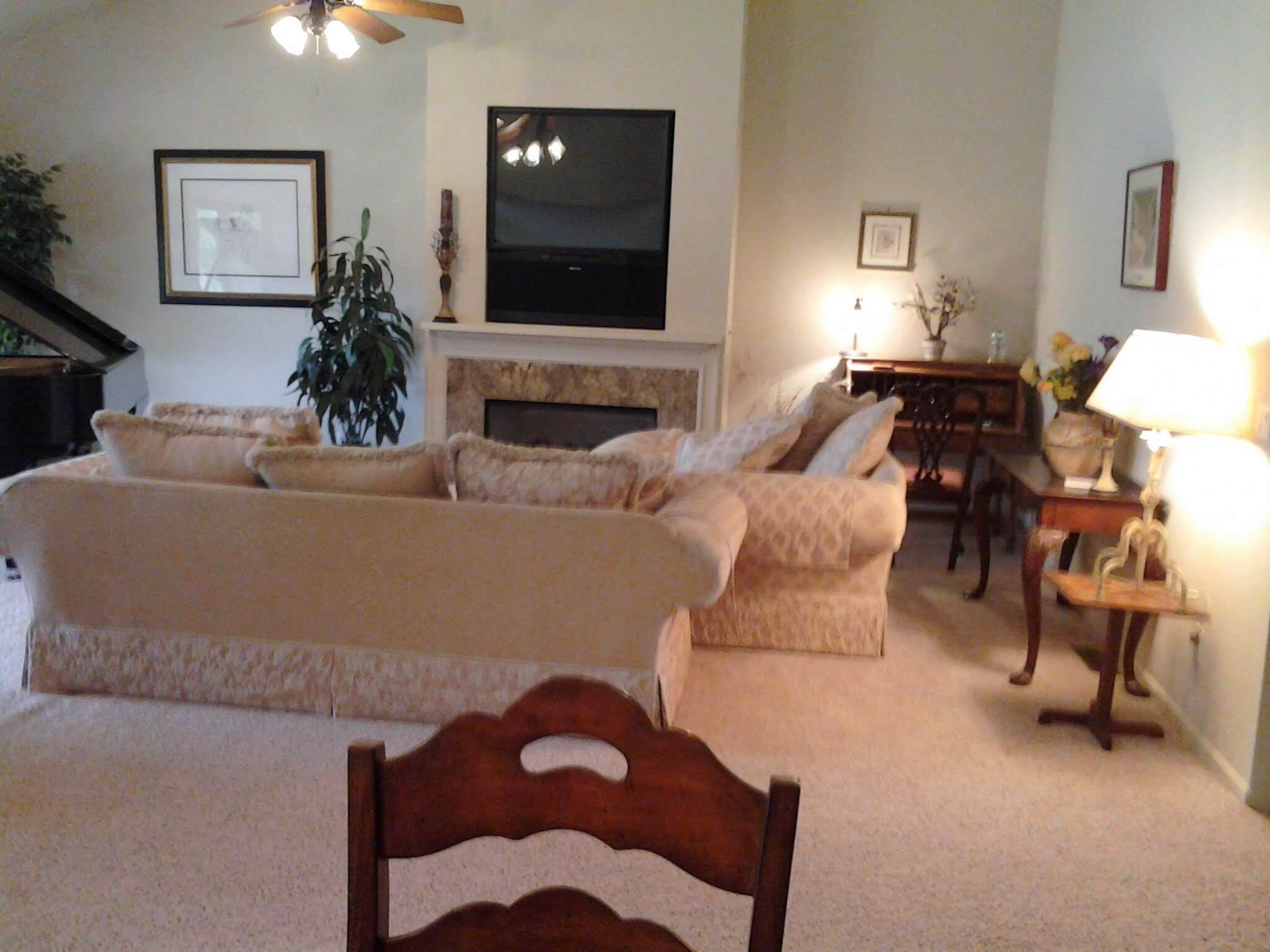 A living room with a sofa set, a television, a fireplace, and a dining area.