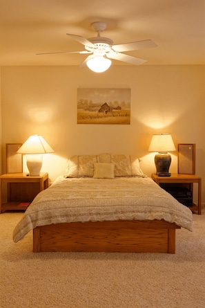 Ein Schlafzimmer mit einem hölzernen Bett, zwei Nachttischen mit Lampen, einem Deckenventilator und einem Bild an der Wand.