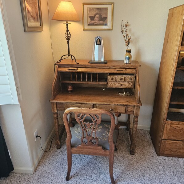 A wooden desk with a lamp, a framed picture, and a vase with branches.