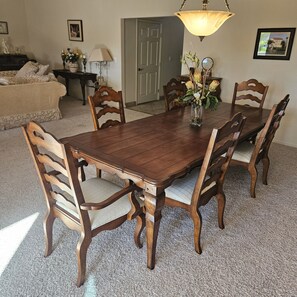 A dining room with a wooden table and chairs, a chandelier, and a door in the background.