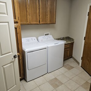 A laundry area with two front-loading washing machines, a sink, and wooden cabinets above.