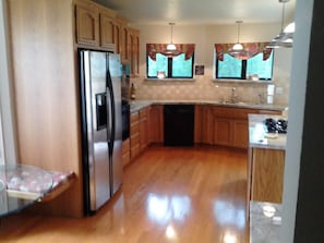 A kitchen with wooden cabinets, a stainless steel refrigerator, a dishwasher, and a glass table. - Waterfront Elegance with Steinway grand (Discovery Bay)