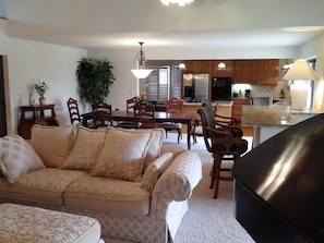 A living room with a sofa and chairs, a dining area with a table and chairs, and a kitchen with cabinets and appliances.