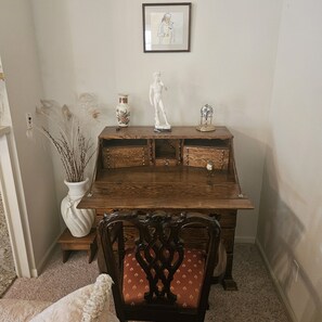 A wooden desk with a vase and a statue, a chair with a patterned cushion, and a framed picture on the wall. - Waterfront Elegance with Steinway grand (Discovery Bay)