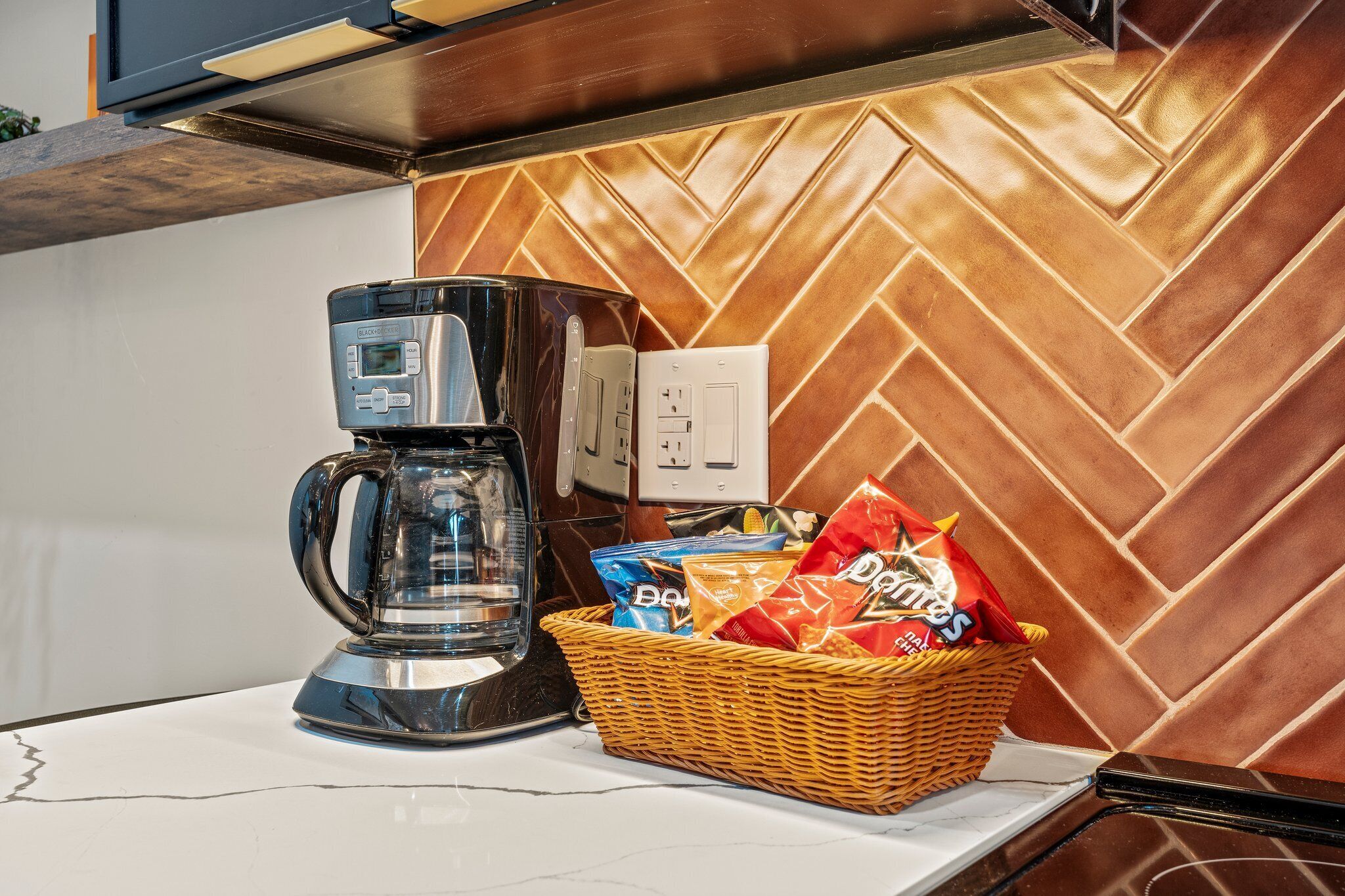 A kitchen counter with a coffee maker, a basket of snacks, and a power outlet.
