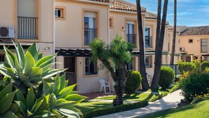 A row of Mediterranean-style buildings with balconies, a paved pathway, and lush greenery.