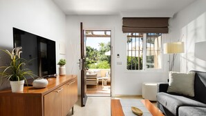 A modern living room with a wooden cabinet, a flat-screen TV, a grey sofa, and a dining area visible through an open door.