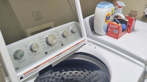 A front-loading washing machine with a control panel, a detergent bottle, and a box of Bounce fabric softener on top.