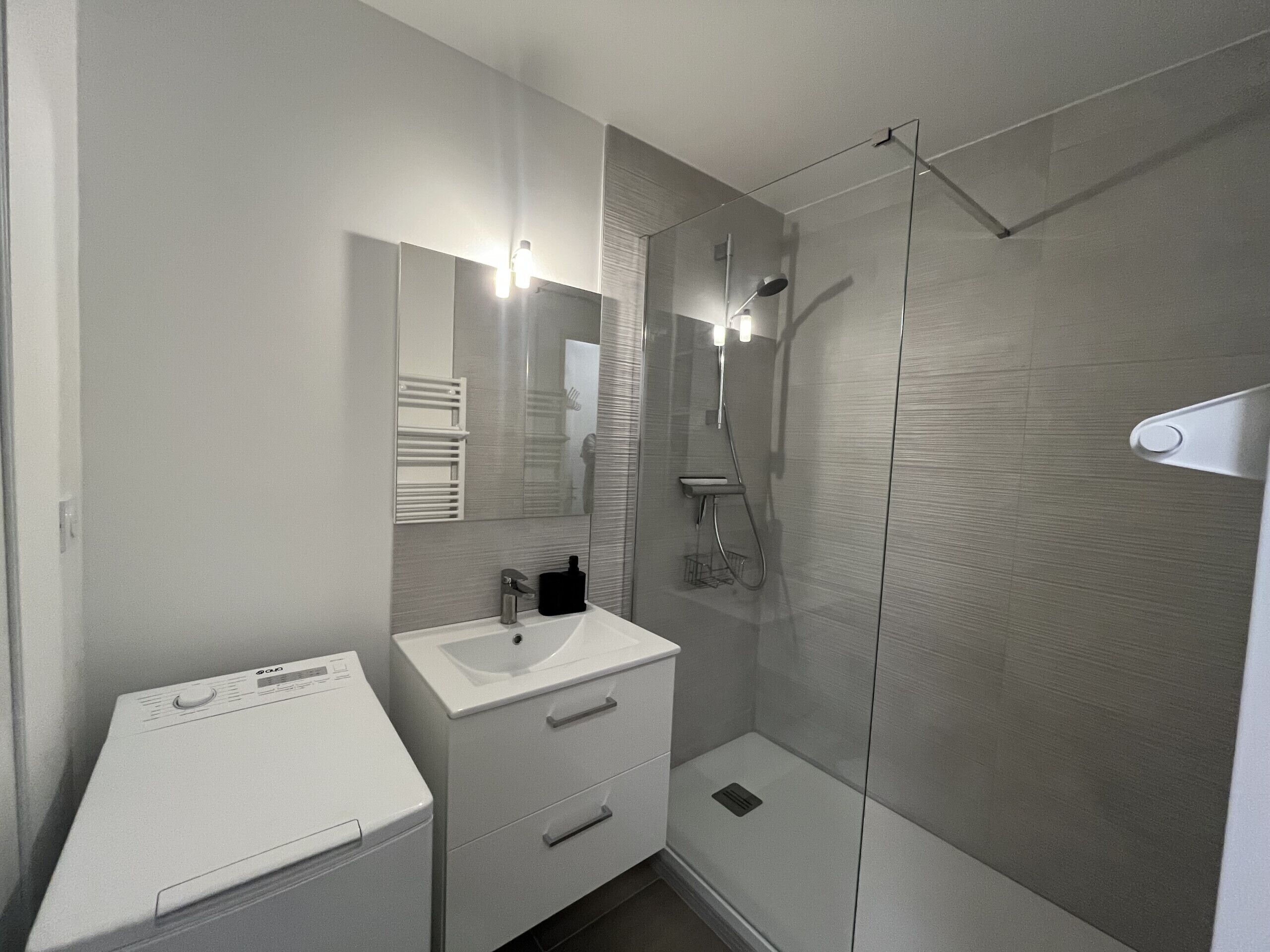 A modern bathroom with a glass shower enclosure, a white sink, and a built-in mirror.