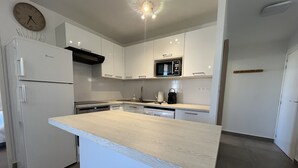 Una cocina moderna con una isla central, armarios blancos, un microondas y un reloj en la pared.