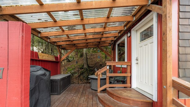 Een houten terras met een overdekte zithoek, een barbecue en een deur naar de binnenruimte.
