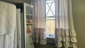 A bathroom with a white towel rack, a shelf with folded towels, and a window with curtains. - The Azalea Room w/ Queen Bed (Woodsfield)