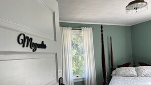 Une chambre à coucher avec un lit à baldaquin, une fenêtre ornée de rideaux blancs et une porte avec une plaque nominative.