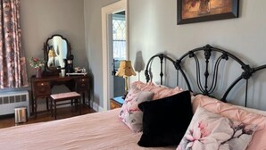 Une chambre à coucher avec un lit, un bureau et une chaise. Il y a un tableau au mur et une fenêtre avec des rideaux.