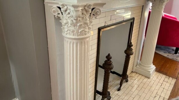 Une cheminée ornée de colonnes blanches décoratives et d’un miroir qui reflète la pièce.