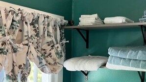 Una habitación con paredes color turquesa, una ventana, un radiador y un estante con toallas dobladas.