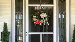Una puerta principal con un adorno floral, una araña y dos paneles de vidrio decorativos.