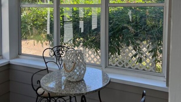 A room with a table and chairs near large windows, a hanging light fixture, and a view of greenery outside.