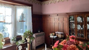 A room with wooden paneling, a radiator, a cabinet with glass doors, and a window with lace curtains.