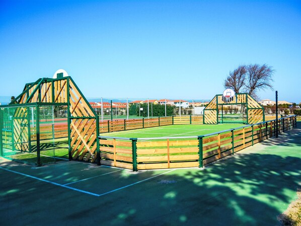 A sports court with a green fence, a basketball hoop, and a netted area.