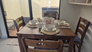 A dining table set with white dishes, glasses, and cutlery, surrounded by wooden chairs with cushioned seats.