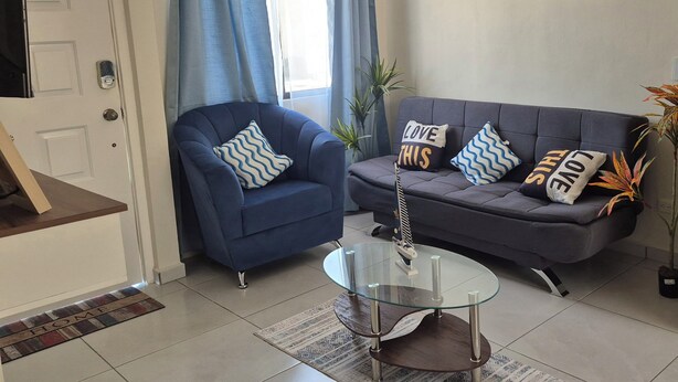 A living room with a blue armchair, a grey sofa, and a glass coffee table.