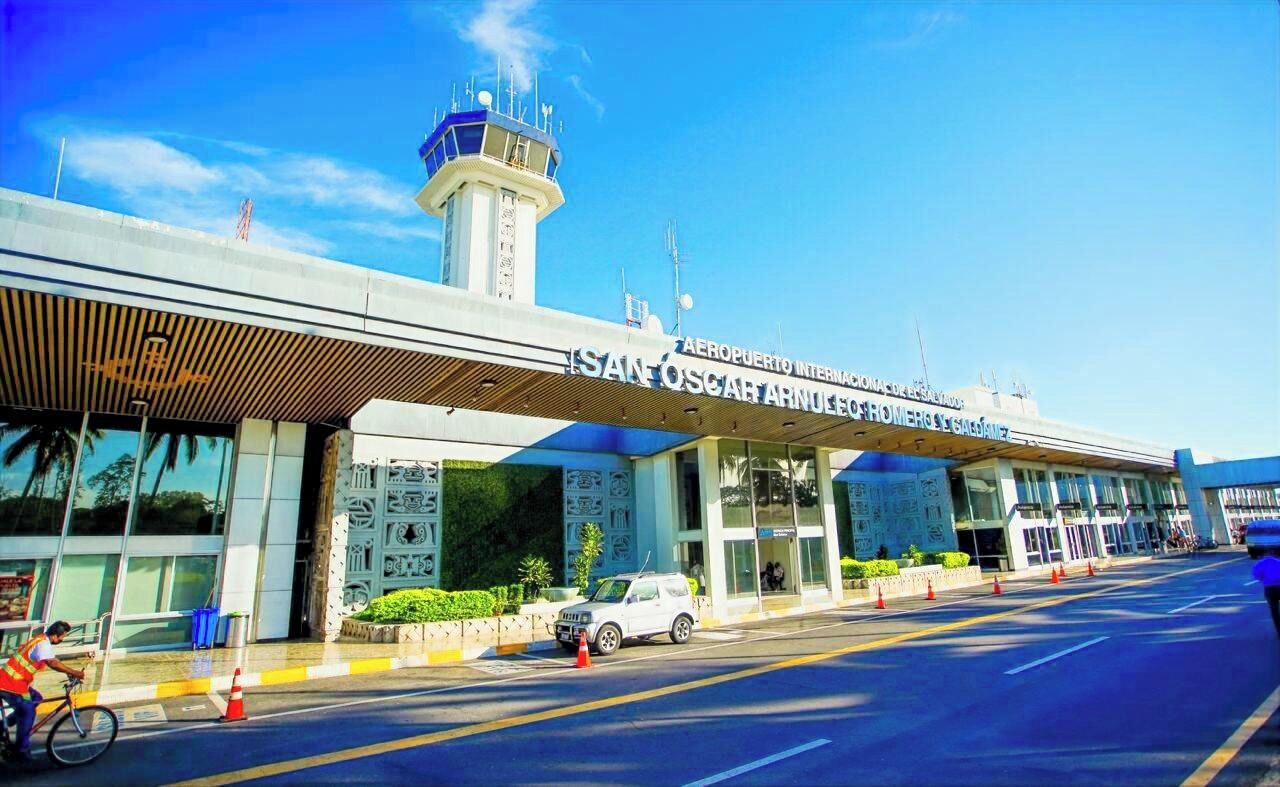 An airport terminal with a modern design, featuring a prominent control tower, clear signage, and a covered waiting area.