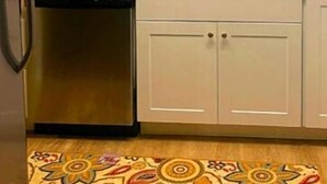 A kitchen with white cabinets, a tiled backsplash, stainless steel appliances, and a patterned rug.