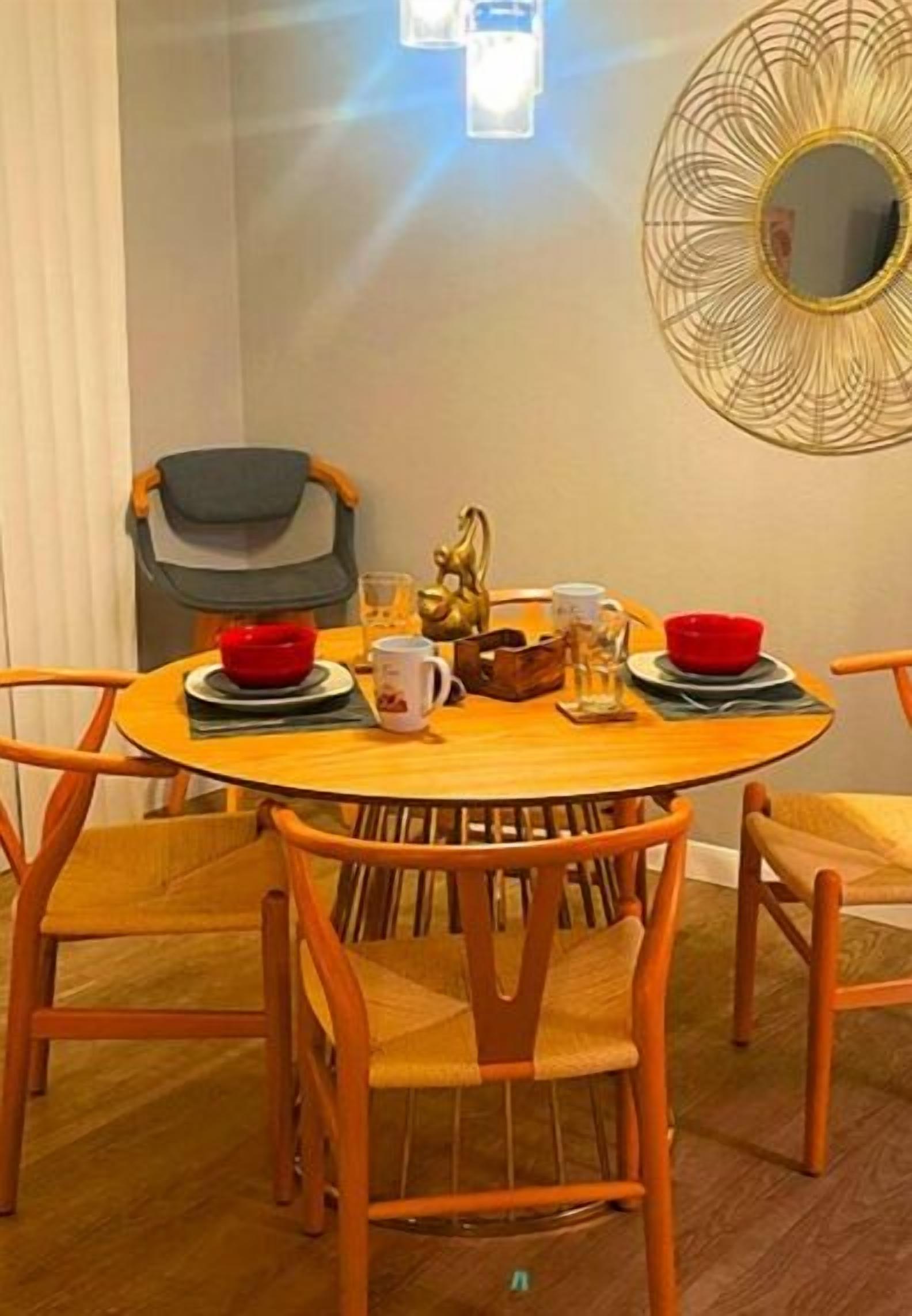 A round wooden dining table with four chairs, a decorative mirror on the wall, and a small statue on the table.