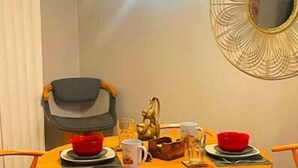 A round wooden dining table with four chairs, a decorative mirror on the wall, and a small statue on the table.