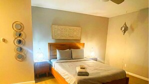A bedroom with a wooden bed, a headboard, bedside lamps, a ceiling fan, and a decorative wall piece.