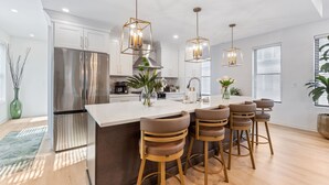 A modern kitchen with a stainless steel refrigerator, white cabinets, and a central island with bar stools. - The Highline - Downtown Rooftop Escape (Columbus)