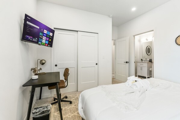 Una habitación de hotel con una cama, un escritorio con computadora, una silla y un televisor montado en la pared.