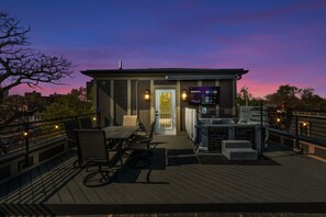 Een terras op het dak met een zithoek, een televisiescherm en een stenen open haard.