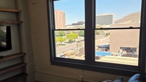 Ein Zimmer mit einem großen Fenster, einem schwarzen Ledersofa und einem Fernseher auf einem Holzboden.