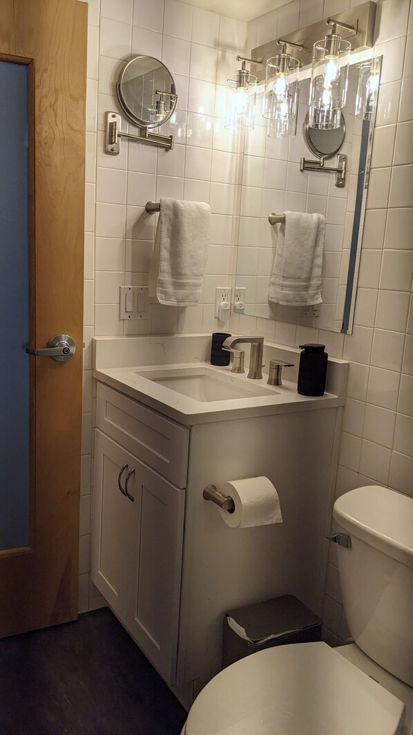 Un baño con lavamanos, espejo, toallero, inodoro y una puerta.
