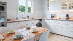 Una cocina moderna con armarios blancos, una mesa de comedor de madera y una cafetera.