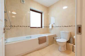 A modern bathroom with a bathtub, toilet, and a window.