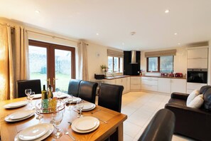 A modern kitchen with white cabinets, a dining area with a wooden table set for four, and a black leather sofa.