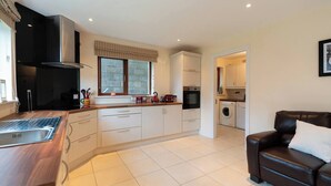 A modern kitchen with a built-in oven, a stovetop, and a sink. There is a dining area with a brown leather couch and a white pillow.