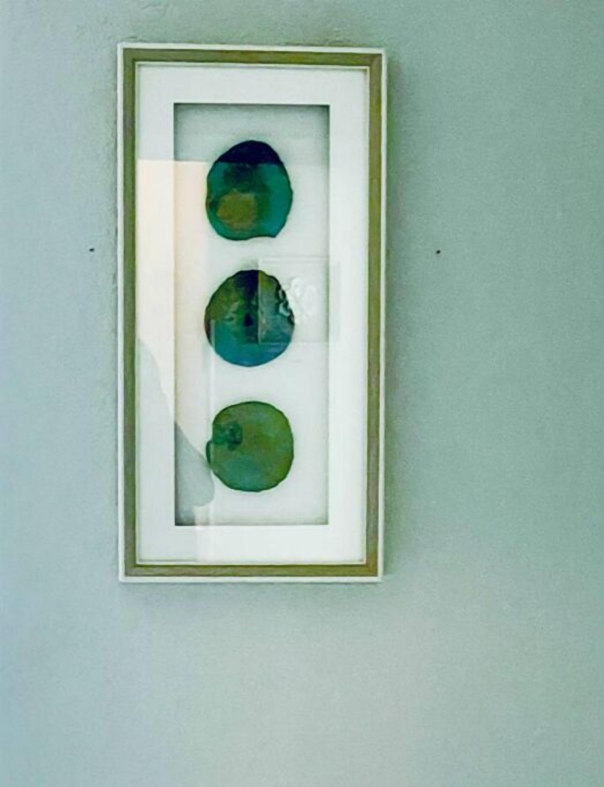 Une œuvre d’art encadrée, composée de trois éléments circulaires, est accrochée au mur.