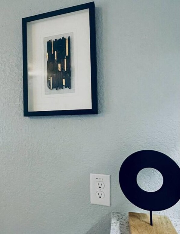 A framed abstract artwork on a light gray wall, a power outlet, and a black circular object on a wooden stand. - The Zen Den-Great location close to downtown (Austin)