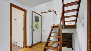Una escalera de madera que sube a una zona de entrepiso con vistas a zonas verdes al exterior.